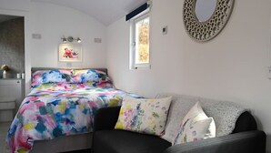 A bedroom with a bed, a grey sofa, a window, and a wall-mounted mirror. - The Carriage near Fort William (Fort William)
