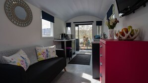 A compact living space with a sofa, a red cabinet, a kitchen area, and a view of the outdoors. - The Carriage near Fort William (Fort William)