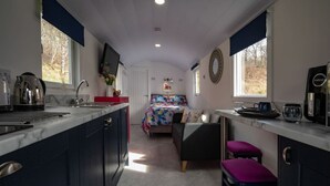 A compact kitchen with a bed in the center, a coffee machine, and a window with a view of trees. - The Carriage near Fort William (Fort William)
