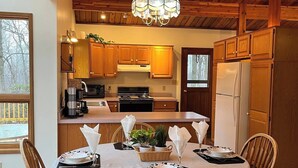 L’intérieur est en bois et comprend une table à manger pour quatre personnes, entourée de chaises en bois. Un lustre est suspendu au plafond, et un ventilateur de plafond est visible.
