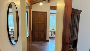 Un couloir au plancher de bois, avec une porte en bois, un miroir et un meuble.