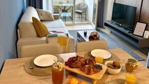 Moderni hotellihuone, jossa on ruokailutila, sohva, televisio ja parveke, jossa on pöytä ja tuolit.