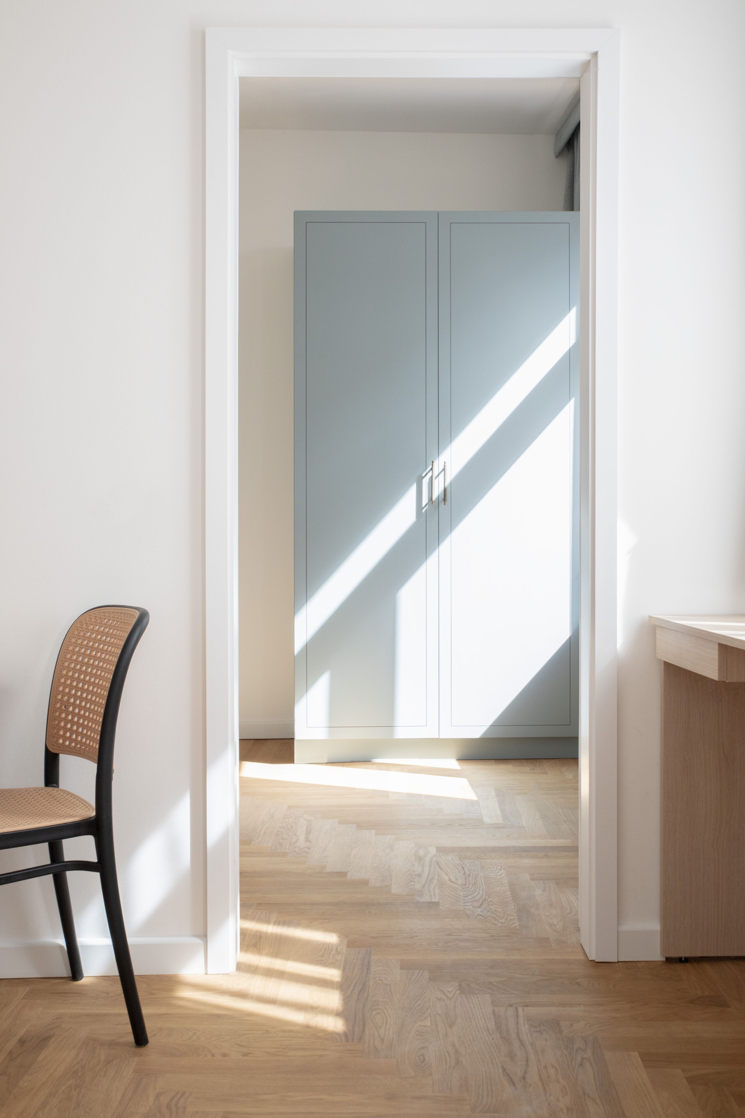 Una habitación con suelo de madera, una silla, un armario y un escritorio.