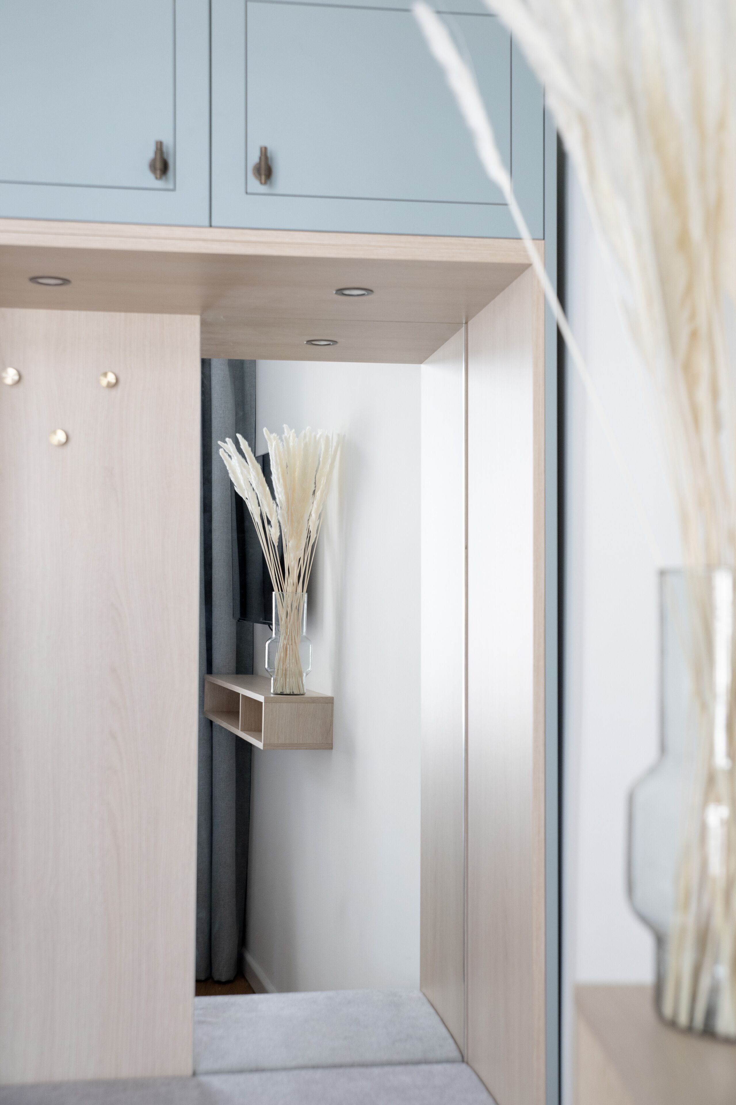 A modern, minimalist room with light wood cabinetry, a built-in shelf with decorative plants, and a neutral color palette.