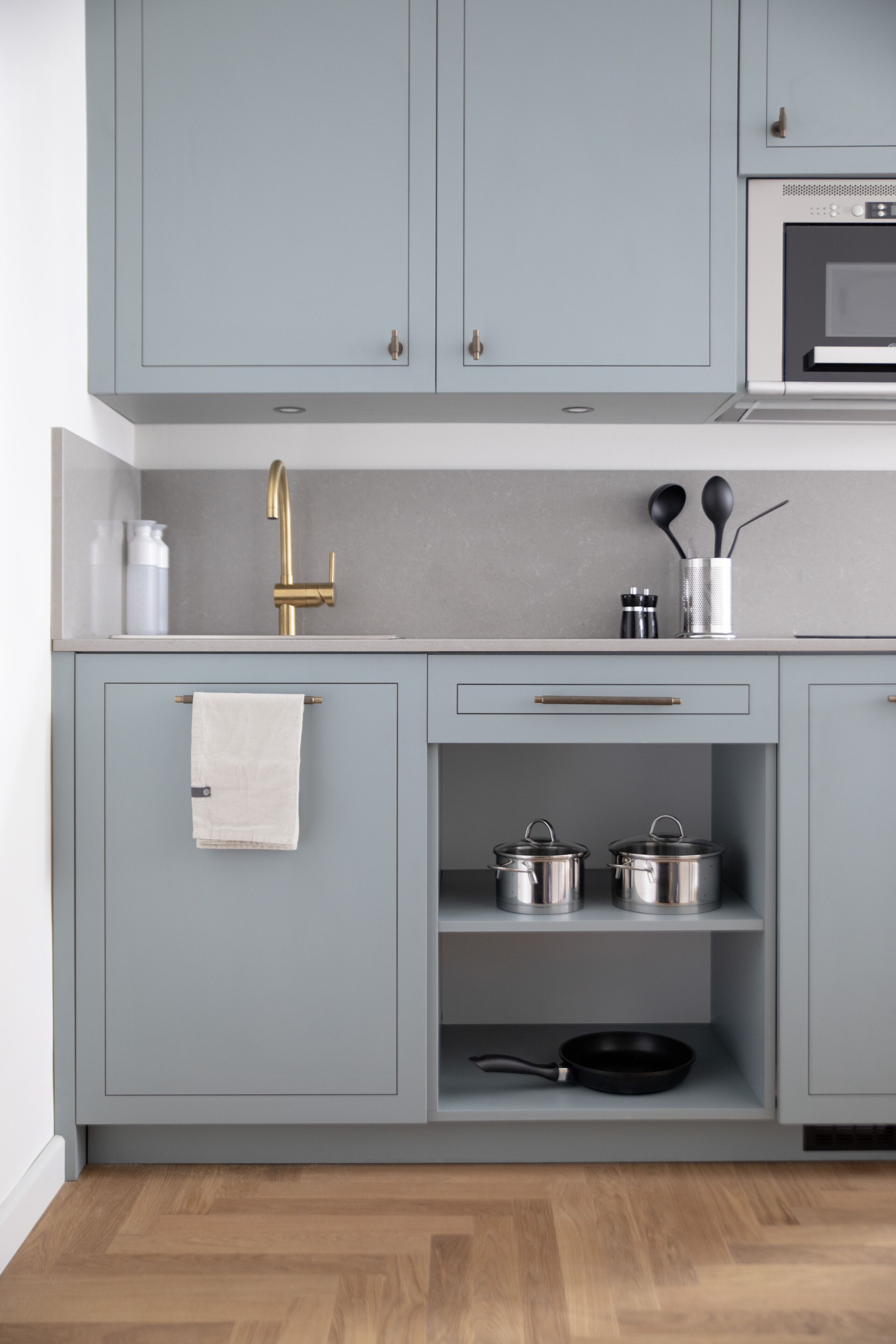 A kitchen with light blue cabinets, a gold faucet, a microwave, and a wooden floor.