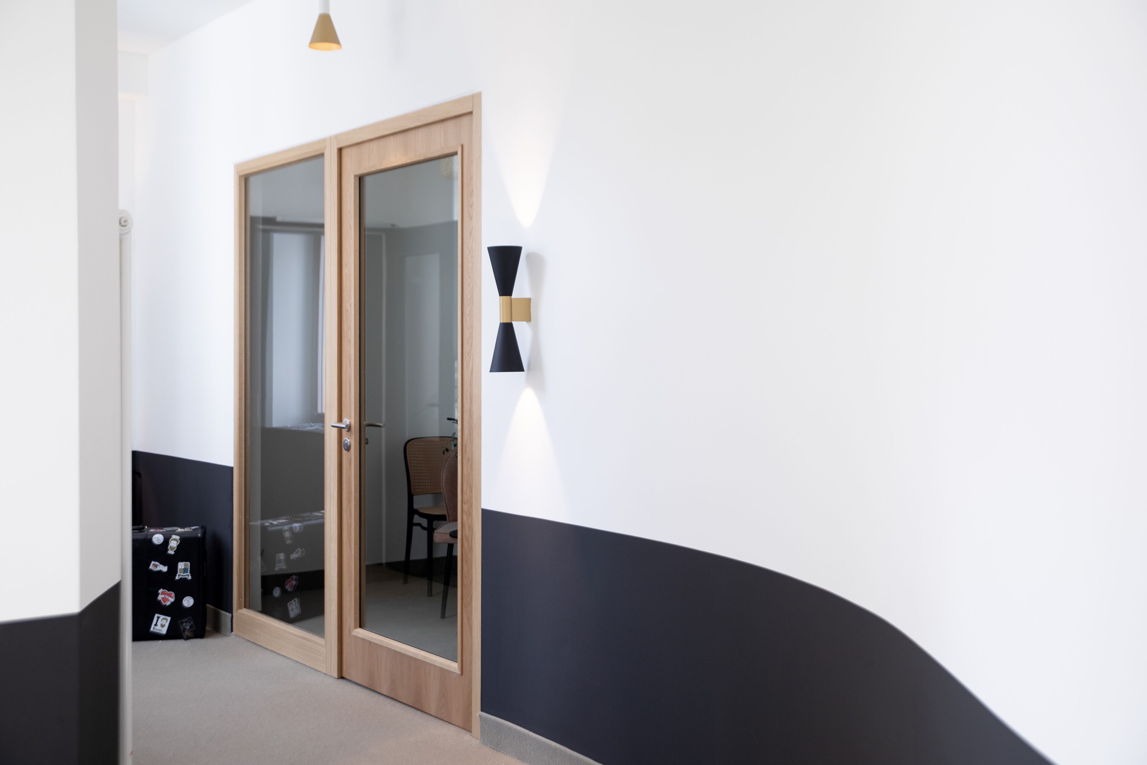A hallway with a wooden door, a wall-mounted light fixture, and a chair.