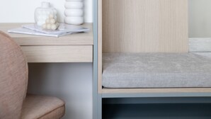 A minimalist room with a wooden wardrobe, a small desk with a white vase and a stack of papers, and a grey cushioned bench. - Bob W Bonn Zentrum (Bonn)