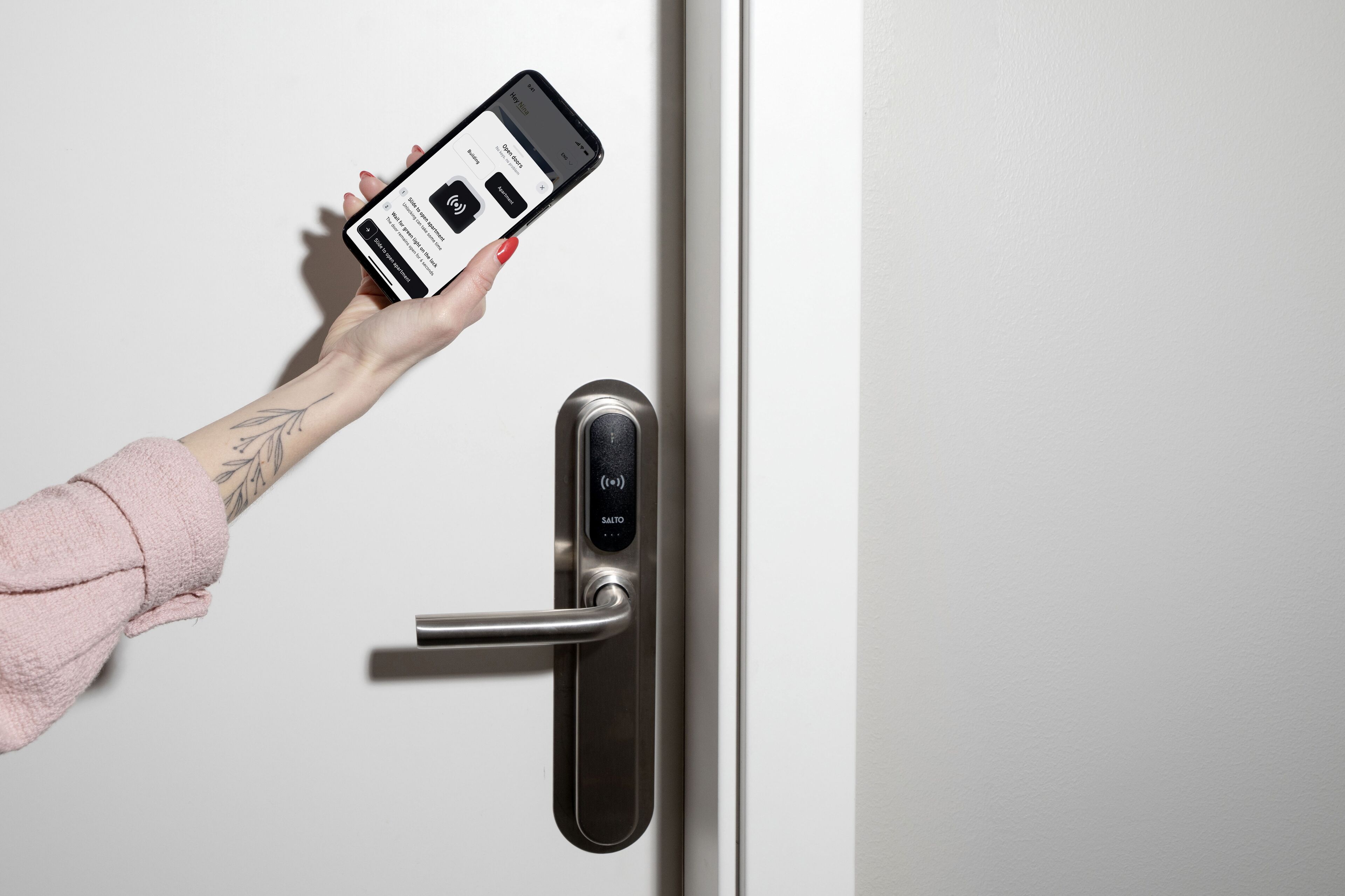 Een hand houdt een smartphone vast nabij een moderne deur met een biometrisch slot.