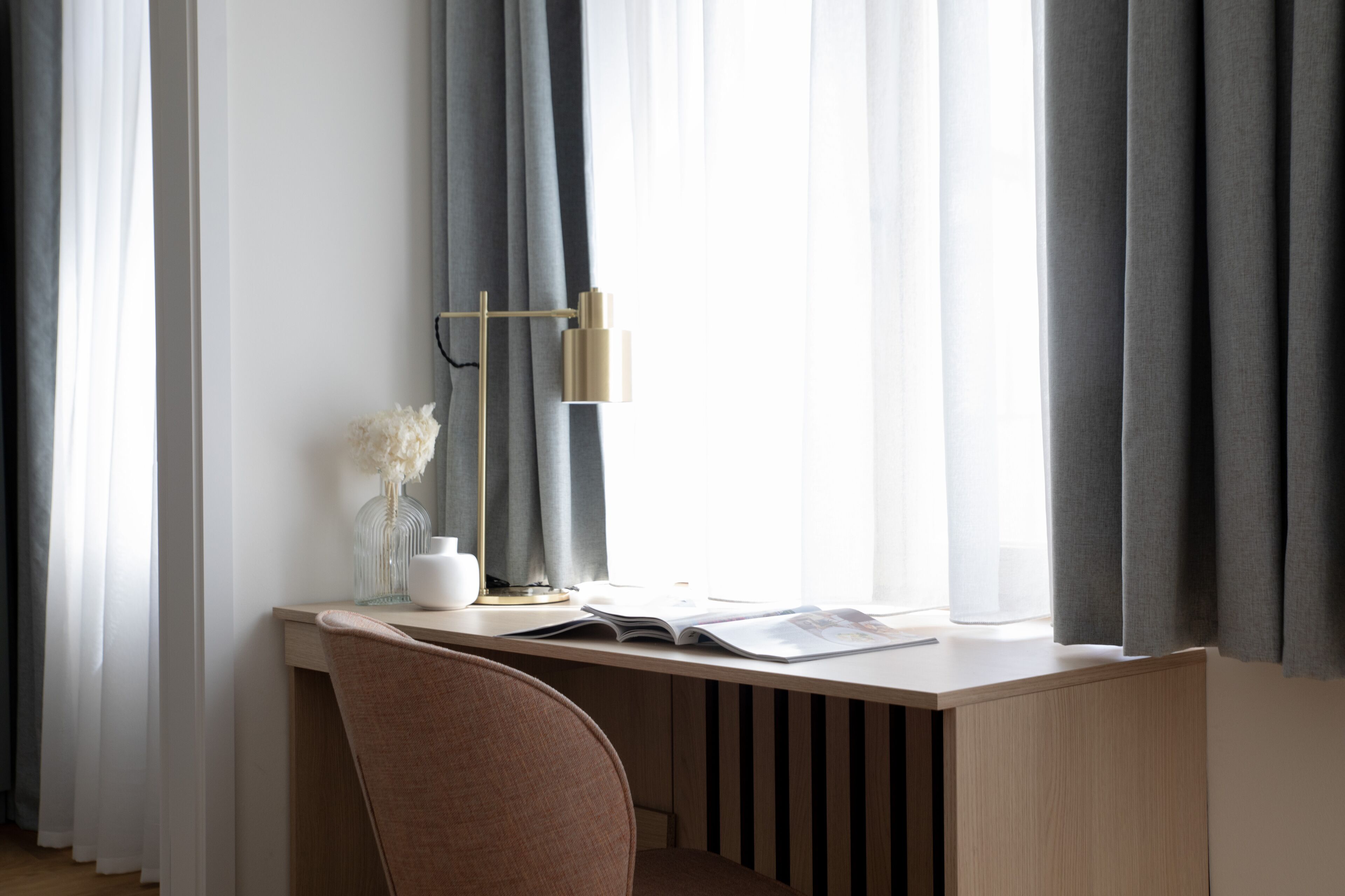 A modern desk with a lamp, a vase with dried flowers, and a magazine.