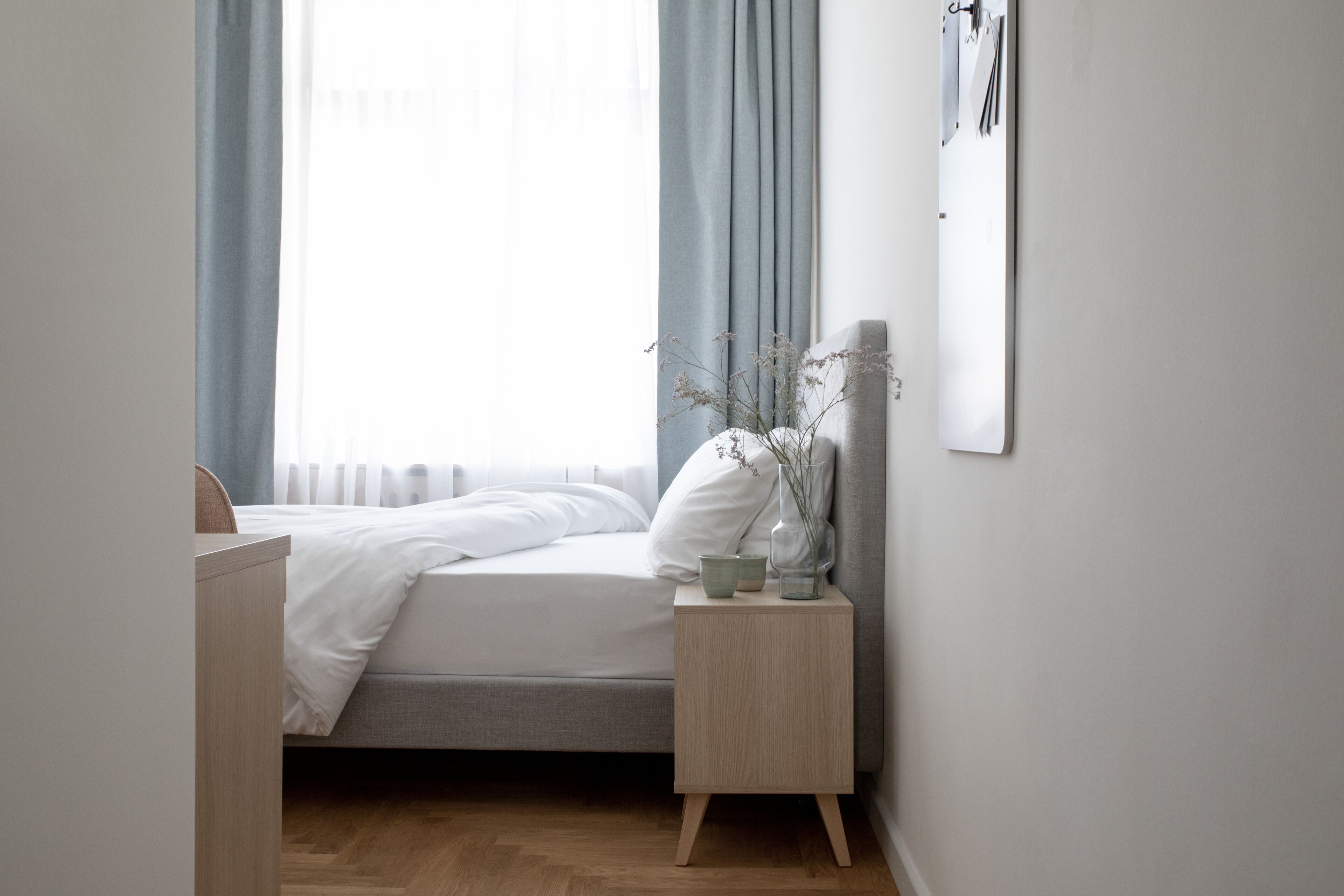 A neatly arranged bedroom with a bed, bedside table, and a window with curtains.