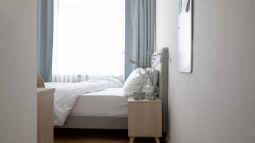 Une chambre bien rangée, avec un lit, une table de chevet et une fenêtre avec des rideaux.