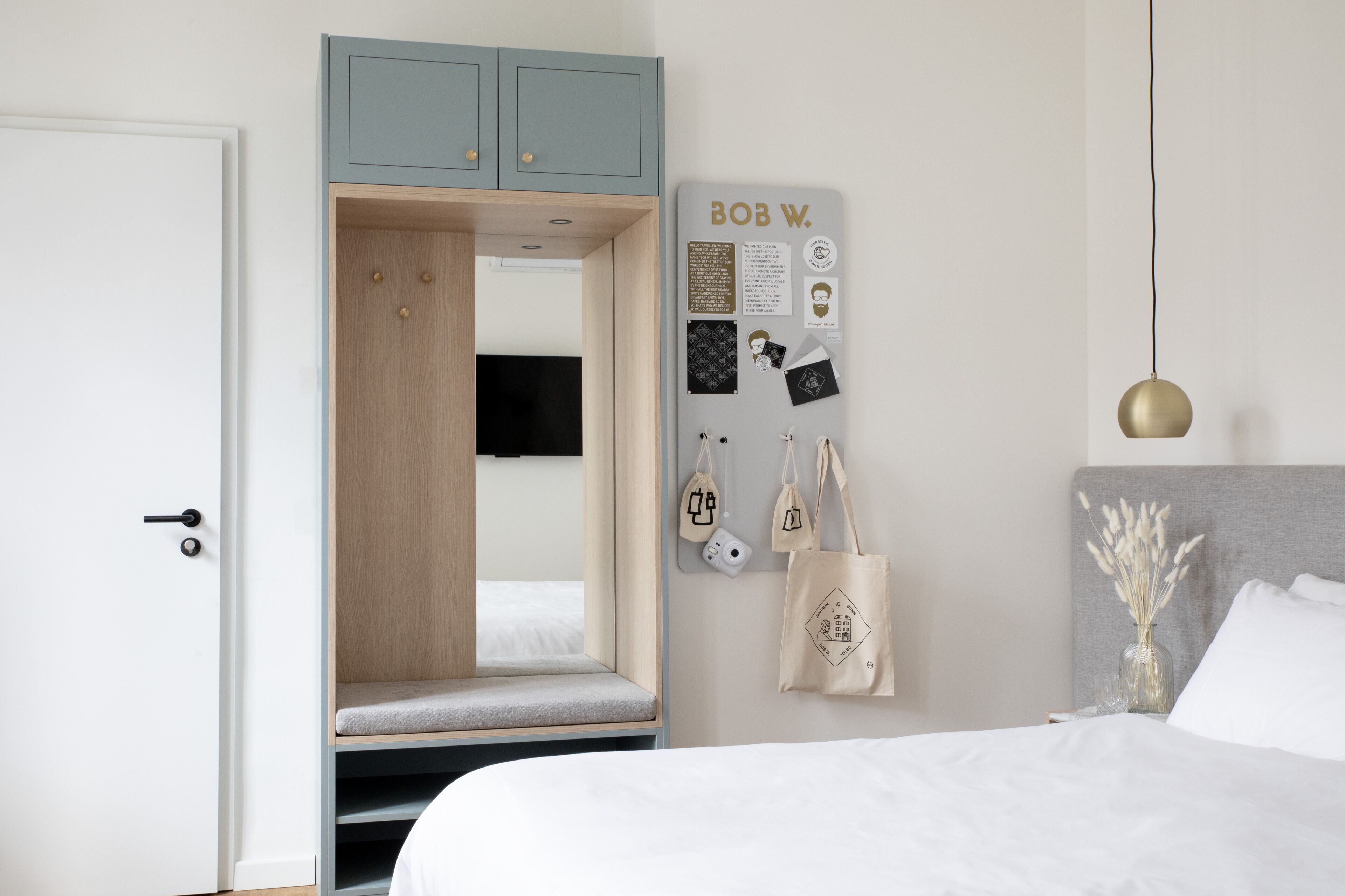 A bedroom with a bed, a wardrobe, a mirror, a bulletin board, and a hanging light fixture.