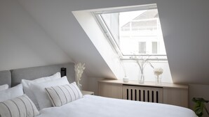 A bedroom with a sloped ceiling, a skylight, a bed with white bedding, a bedside table, and a radiator. - Bob W Bonn Zentrum (Bonn)