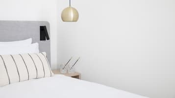 A neatly made bed with a striped pillow, a bedside table with two glasses, and a hanging pendant light.