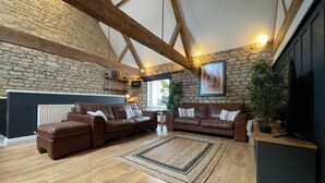 A spacious living room with a stone wall, wooden beams, a fireplace, and leather sofas.