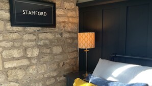 A bedroom with a stone wall, a bed with blue and yellow pillows, a lamp, and a sign that reads "STAMFORD".