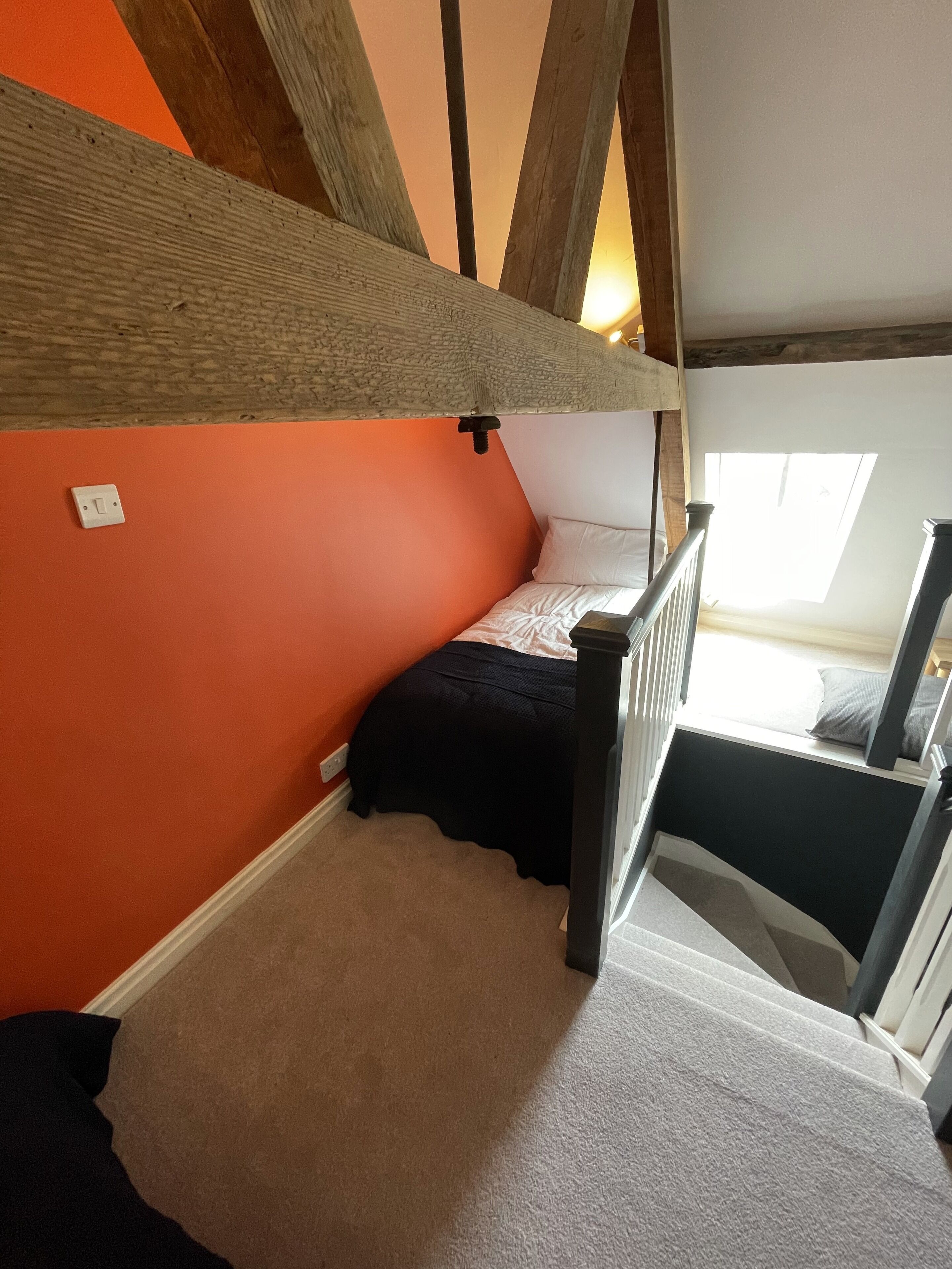 A bedroom with a sloped ceiling, a bunk bed, a window, and a staircase.