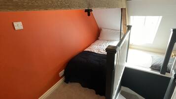 A bedroom with a sloped ceiling, a bunk bed, a window, and a staircase.