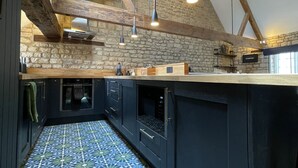A kitchen with exposed wooden beams, a stone wall, and a tiled floor.