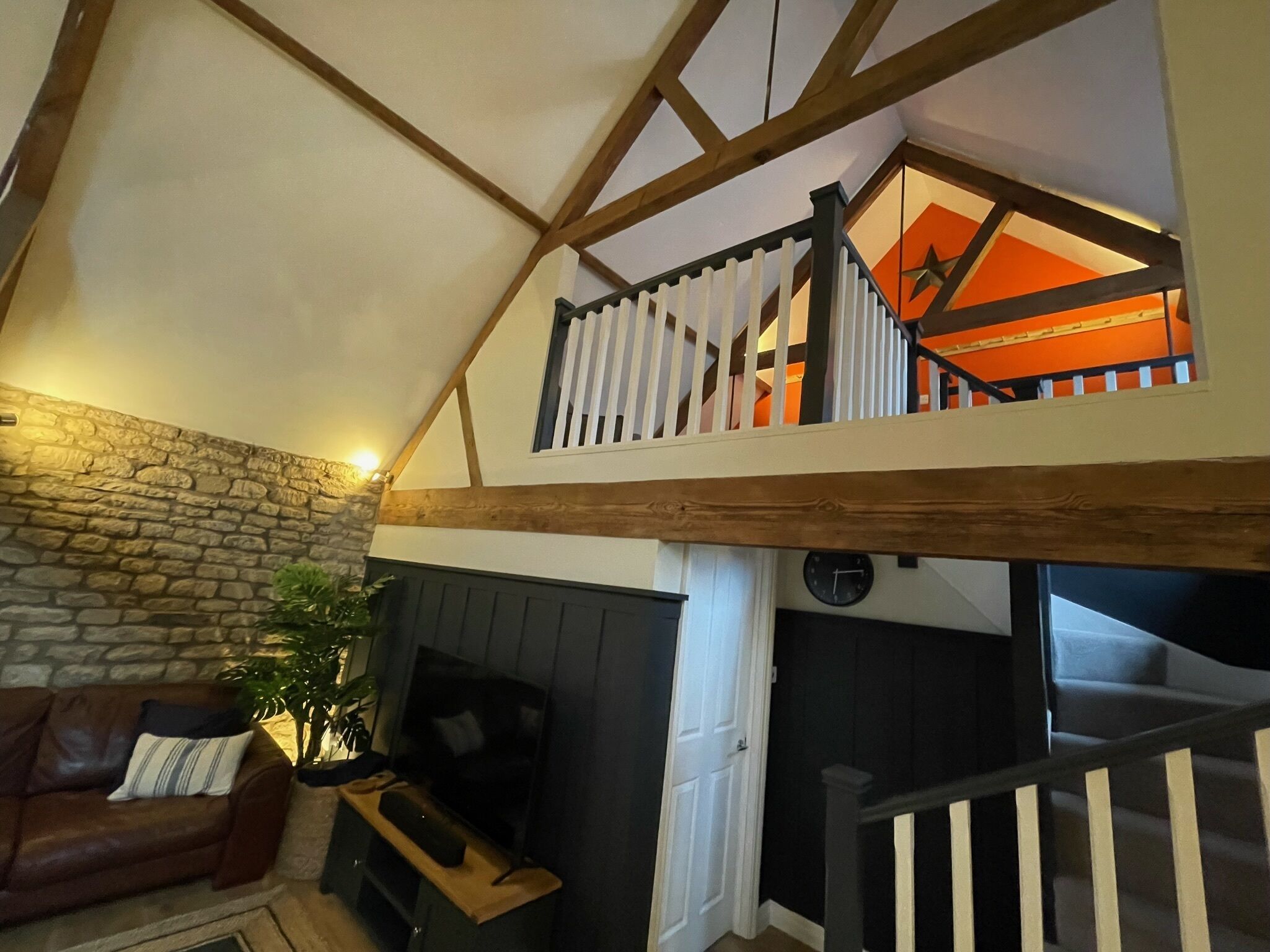 Un salón estilo loft con vigas de madera expuestas, pared de piedra, chimenea, sofá y una escalera que lleva a un nivel superior con un adorno en forma de estrella.
