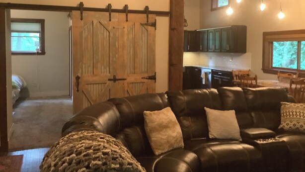 Un soggiorno con un divano in pelle, una porta di legno in stile rustico e una cucina sullo sfondo.