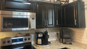Una cucina con mobili neri, un forno a microonde in acciaio inox, una macchina da caffè e un tostapane.