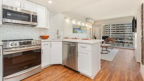 A modern kitchen with white cabinetry, stainless steel appliances, and a wooden floor. - Tropical City Escape at Ilikai Hotel by the Beach w/Great Building Amenities (Honolulu)
