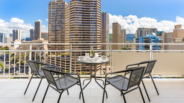 A balcony with two chairs and a table, overlooking a cityscape with tall buildings. - Tropical City Escape at Ilikai Hotel by the Beach w/Great Building Amenities (Honolulu)
