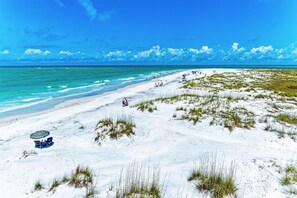 A beach with white sand, a clear blue sky, and a few people.
