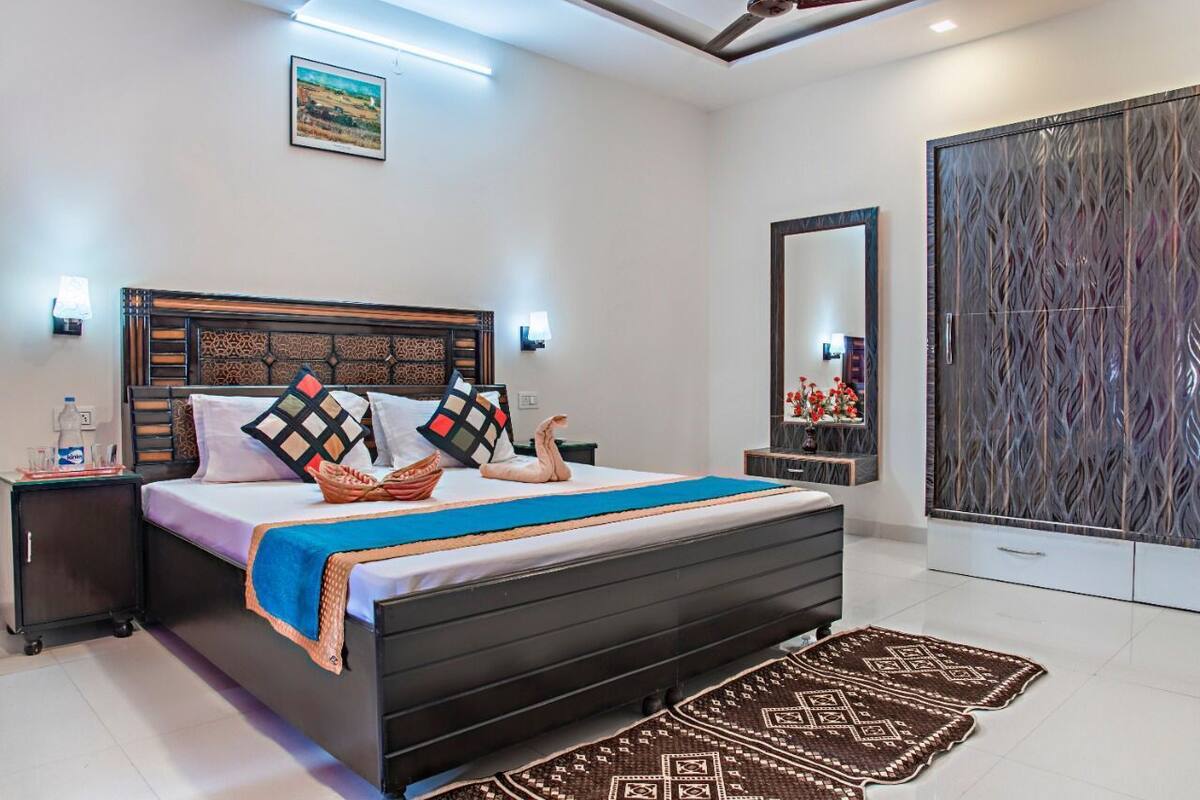 A modern bedroom with a large bed, a nightstand, a dresser, a mirror, and a wardrobe.