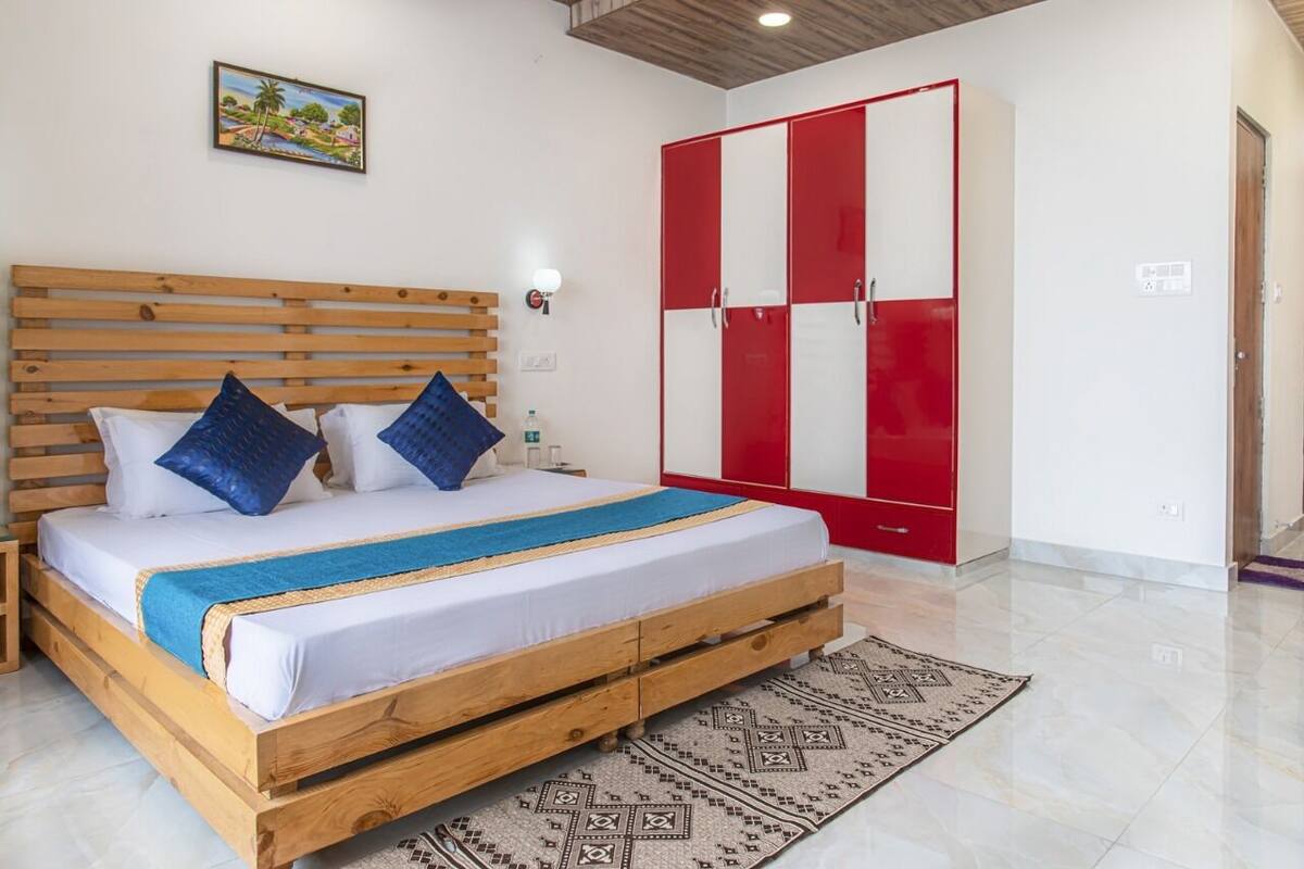 A bedroom with a wooden bed, a red and white wardrobe, a patterned rug, and a wall-mounted light.