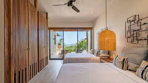 Une chambre moderne avec deux lits, un ventilateur de plafond et une grande fenêtre donnant sur l’extérieur.