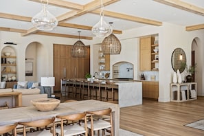 A spacious living area with a wooden dining table, multiple seating options, and a kitchen area with wooden cabinets and a central island.