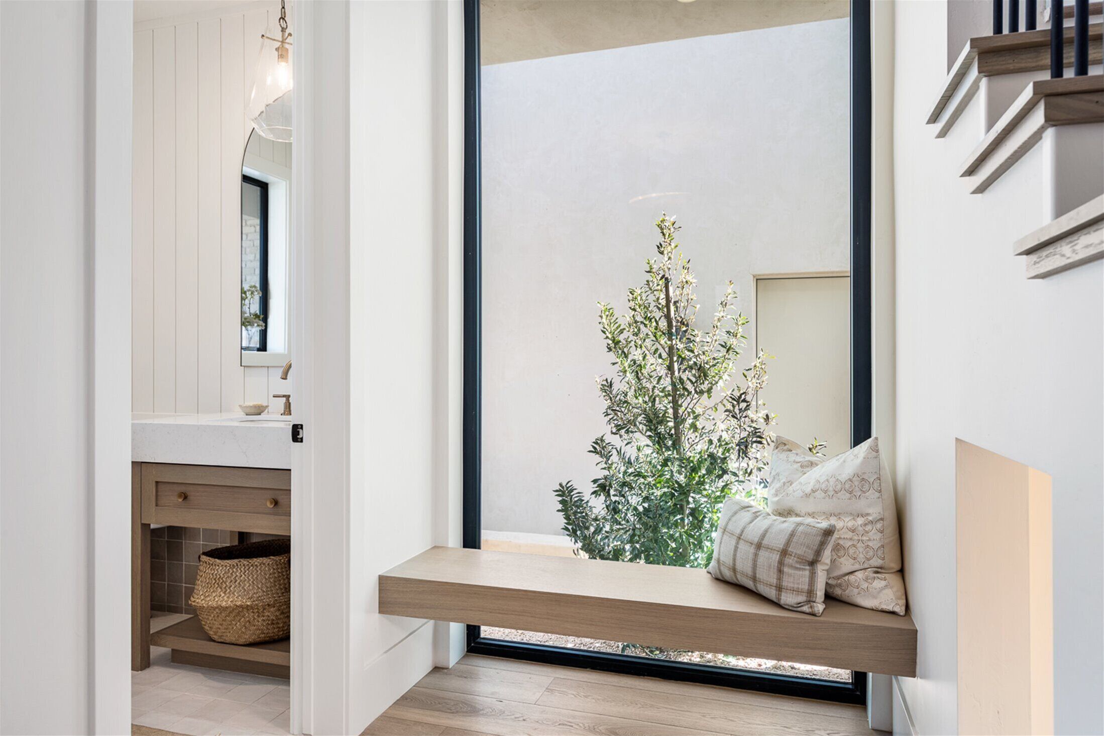 A modern bathroom with a built-in bench, a large window, and a view of a tree outside.