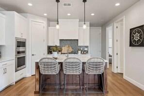 A modern kitchen with white cabinetry, a central island with bar stools, stainless steel appliances, and pendant lighting.