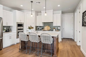 A modern kitchen with white cabinets, a central island with bar stools, a microwave, and a sink.