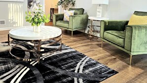 A modern living room with a green sofa, a round coffee table, and a decorative clock on the wall. - Luxury 4 Bed Room Near Stadium (Kansas City)