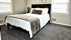 A bedroom with a bed, a nightstand, a lamp, and a painting on the wall. - Luxury 4 Bed Room Near Stadium (Kansas City)