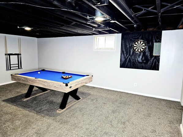 A pool table in a room with a dartboard and a window.