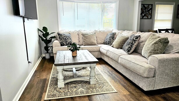 A living room with a sectional sofa, a coffee table, and a large window. - Luxury 4 Bed Room Near Stadium (Kansas City)
