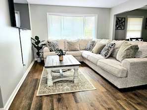 A living room with a sectional sofa, a coffee table, and a large window.