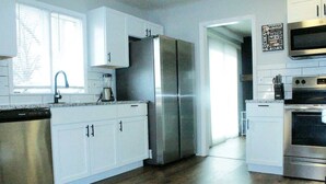 A modern kitchen with stainless steel appliances, white cabinetry, and a wooden floor. - Luxury 4 Bed Room Near Stadium (Kansas City)