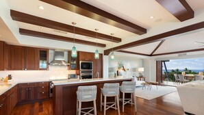 A modern kitchen with wooden cabinets, a large island with bar stools, and a view of the ocean.