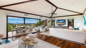 A spacious living room with a large window, a ceiling fan, and a view of the ocean.
