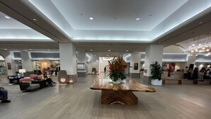 Eine großzügige Lobby mit einem zentralen Holztisch, Sitzbereichen und einer Rezeption.