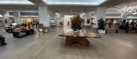 A spacious lobby with a central wooden table, seating areas, and a reception desk.