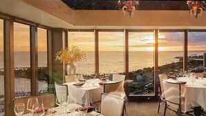 Ein Restaurant mit gedeckten Tischen, großen Fenstern mit Meerblick und einer Kronleuchter an der Decke.