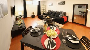 Un comedor con una mesa preparada para dos personas, un sofá y un televisor al fondo.
