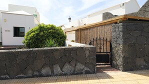Un muro de piedra, un portón de madera y un edificio blanco con un ventanal verde.