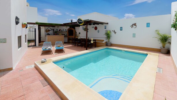 Una piscina con sillas de descanso, una pérgola y una zona de bar.